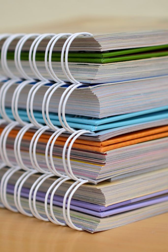 pexels-photo-272980-272980 A colorful stack of spiral-bound notebooks neatly placed on a wooden desk. Ideal for educational themes.