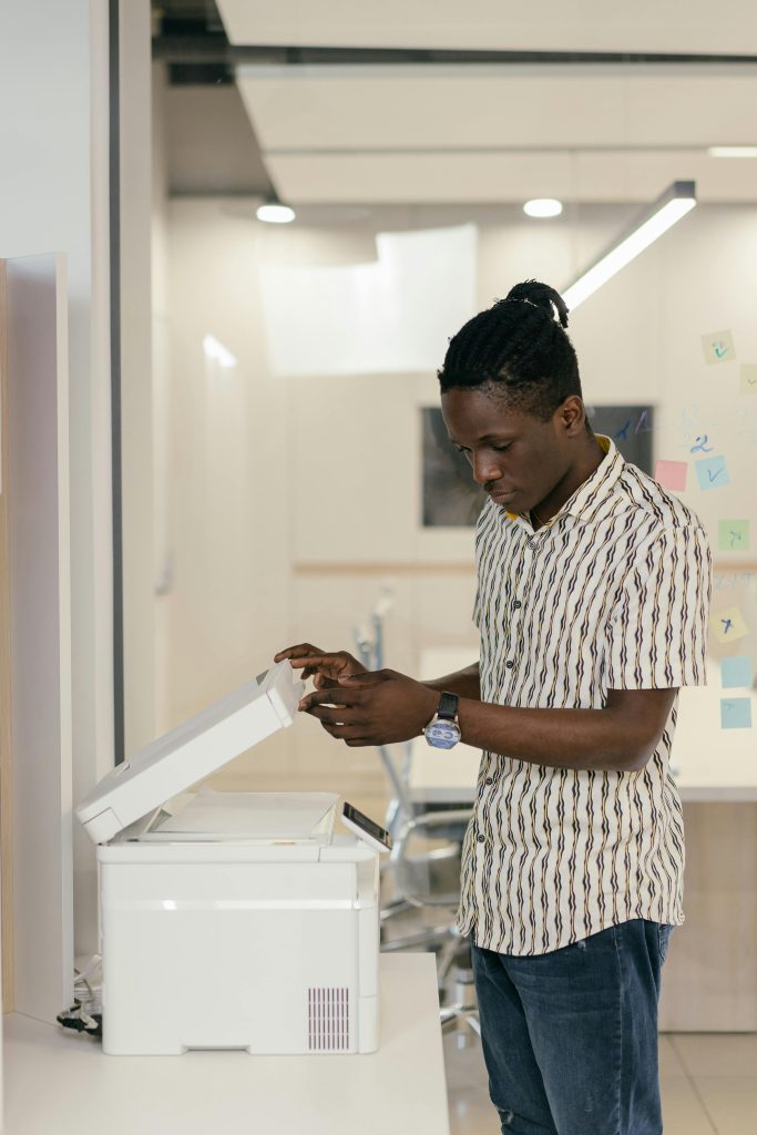 pexels-photo-9301888-9301888 A young black man operates a photocopier in a modern office setting.
